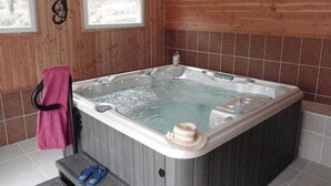 Un bain à remous dans une pièce aux murs lambrissés, avec une fenêtre et un porte-serviettes.