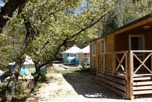 A wooden cabin with a porch, surrounded by trees and a gravel path. - Camping 2 étoiles - Piscine  - ccbfidb (Vernet-les-Bains)