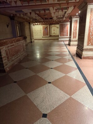 Un pasillo amplio con piso a cuadros, columnas de mármol y techo decorativo.