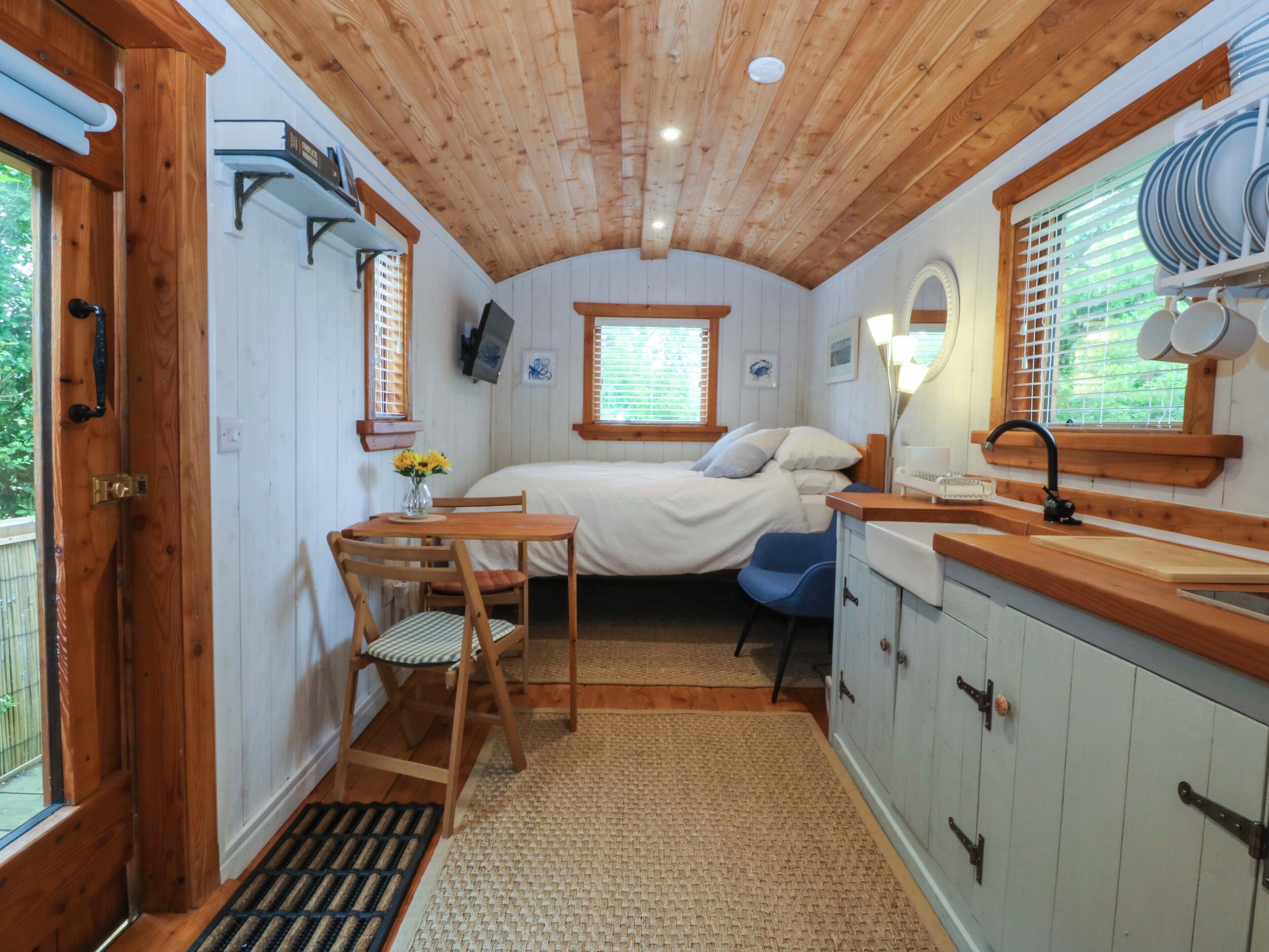 A compact room with a bed, a small desk with a chair, a window with blinds, a sink, and a cabinet.