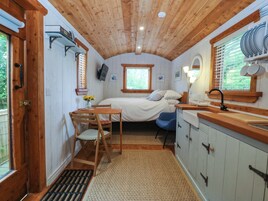 Habitación pequeña con cama, un escritorio con silla, ventana con persianas, lavamanos y armario.