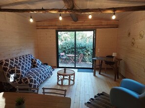 A wooden interior with a sofa, round table, and chairs, a large sliding glass door leading outside, and a small table with a lamp.