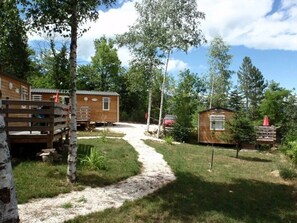A campsite with wooden cabins, a gravel path, and surrounding trees.