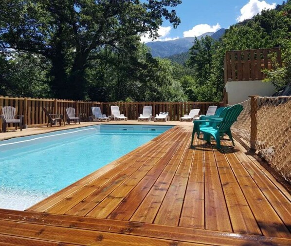 A wooden deck with a swimming pool, surrounded by chairs and a wooden fence.