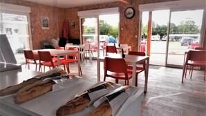 Interior de un restaurante con mesas y sillas, una barra con pan y vistas a través de puertas de cristal.