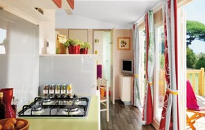 A compact kitchen with a gas stove, a refrigerator, and a dining area with a chair and table. - Camping 3 étoiles - Piscine  - ccbgaig (Loubeyrat)