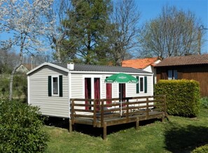 A small, single-story building with a porch, a green awning, and a wooden fence. - Camping 3 étoiles - Piscine  - ccbgaig (Loubeyrat)