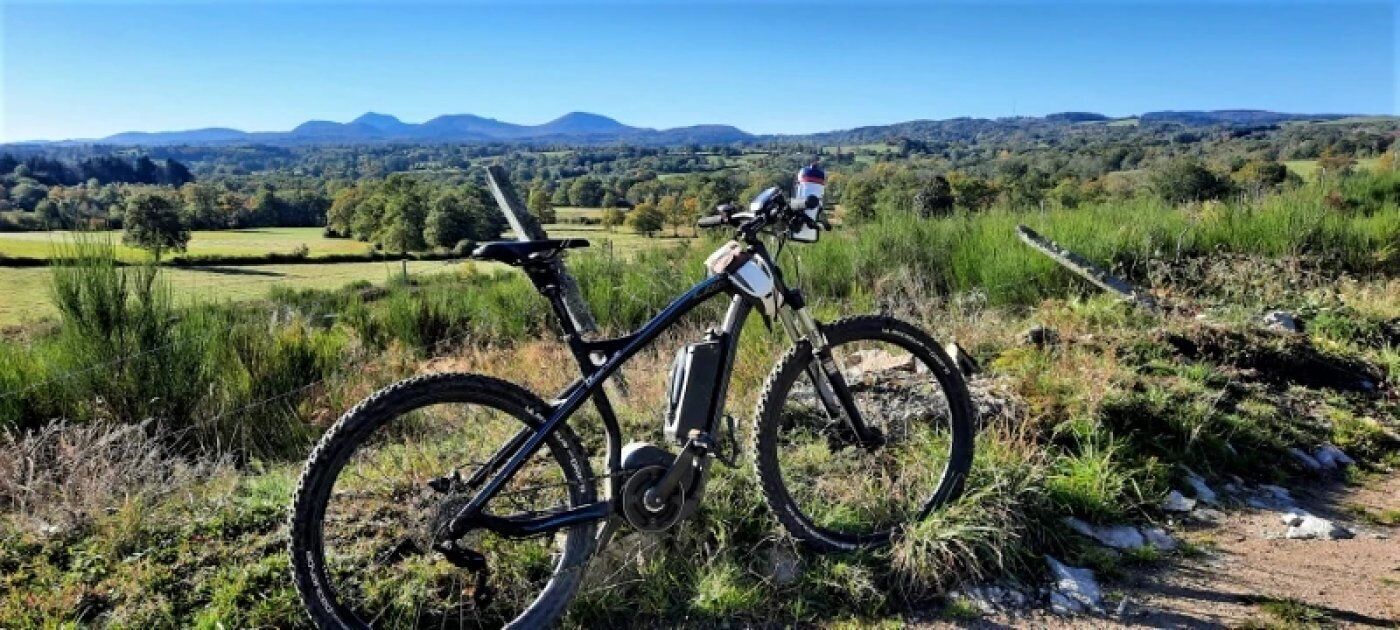 Un vélo tout-terrain est garé sur un sentier de terre, offrant une vue panoramique sur une vallée et des montagnes lointaines.