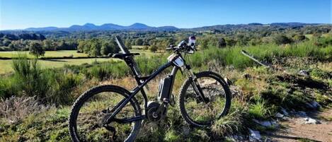 Un vélo tout-terrain est garé sur un sentier de terre, offrant une vue panoramique sur une vallée et des montagnes lointaines.