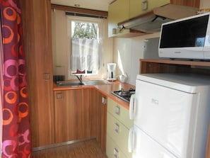 Eine kleine Küche mit Mikrowelle, Herd, Spüle und einem Fenster mit Vorhängen.