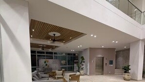 En rymlig entréhall med högt i tak, en modern soffa, flätade stolar, en receptionsdisk och en dörrmatta med texten ”COUTURI”.
