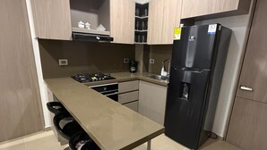 Ett modernt kök med en central köksö, rostfria vitvaror och ljusa träskåp.