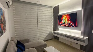 Ett modernt vardagsrum med en platt-TV, en grå soffa och ett litet soffbord.