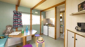 Een kleine keuken met een koelkast, een koffiezetapparaat en een eethoek met een tafel en stoelen.