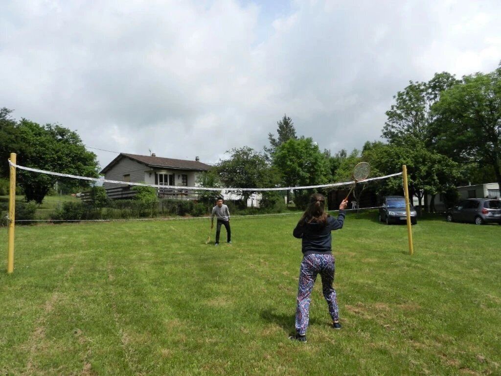 An outdoor netted area with a grassy field, a house in the background, and a clear sky.