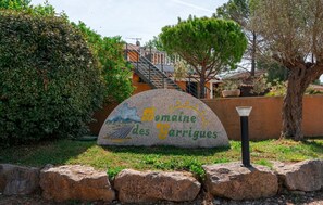 A stone sign with 'Domaine des Garrigues' text, surrounded by greenery and a stone wall. - Camping 3 étoiles - Piscine  - ccbgbde (Grospierres)