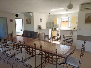 Ein Essbereich mit einem langen Tisch und Stühlen, eine Küche mit Geräten und ein Waschbereich.