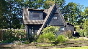 A house with a steeply pitched roof, a small window, and a wooden fence in the foreground. - Modern, cozy vacation home with a fireplace, sauna, and large garden (Winsen (Aller))