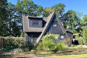 Ein Haus mit einem steilen Satteldach, einem kleinen Fenster und einem Holzzaun im Vordergrund.