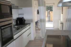 Una cocina moderna con electrodomésticos de acero inoxidable, una cafetera y vistas al jardín trasero por una puerta abierta.