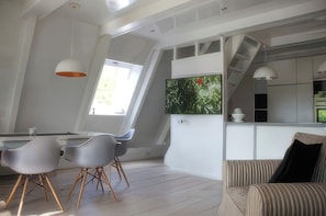 Eine moderne Küche mit Fernseher, ein Essbereich mit Stühlen und eine Treppe.