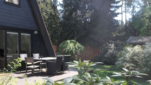 A patio with a table and chairs, surrounded by greenery and a wooden fence. - Modern, cozy vacation home with a fireplace, sauna, and large garden (Winsen (Aller))