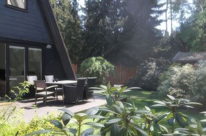 Eine Terrasse mit Tisch und Stühlen, umgeben von Grünpflanzen und einem Holzzaun.