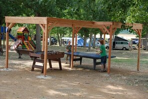 En lekställning i trä med en rutschkana och ett bordtennisbord i en park.