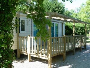 Eine erhöhte Holzterrasse mit überdachter Veranda, umgeben von viel Grün.
