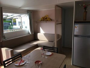 Eine kompakte Küchenzeile mit Kühlschrank, einem Esstisch mit Stühlen, einer Bank und einem Fenster mit Vorhängen.