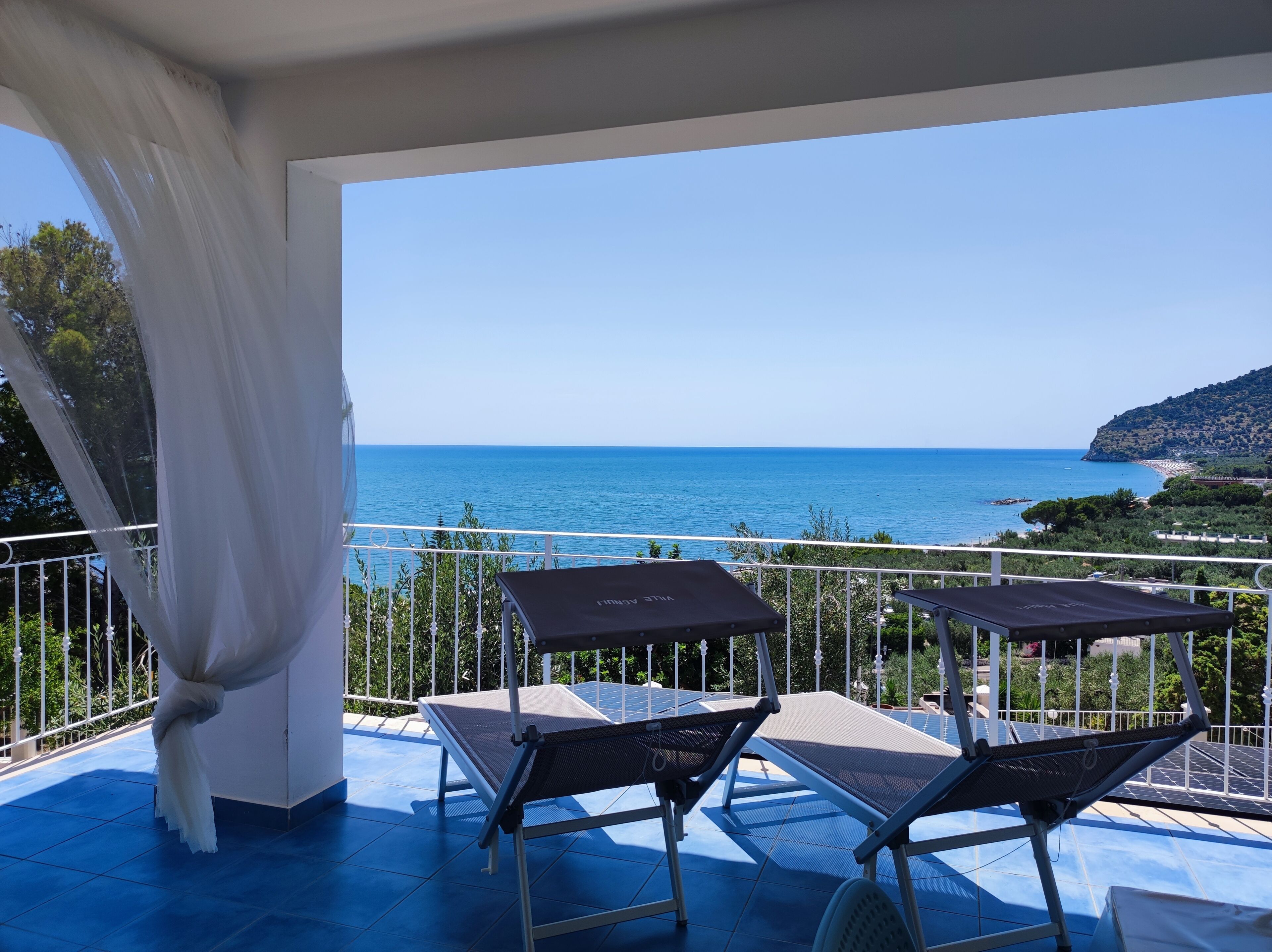 Un balcon avec deux chaises longues, un rideau blanc et une vue sur la mer.