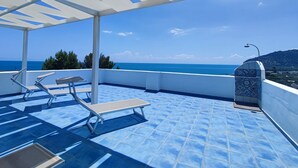 Área externa coberta com piscina, espreguiçadeiras e vista para o mar.