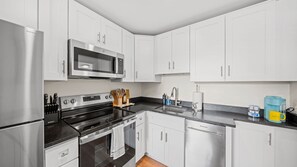 Uma cozinha moderna com eletrodomésticos de aço inoxidável, armários brancos e bancada preta.