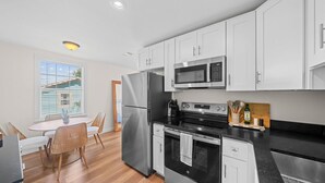 A modern kitchen with stainless steel appliances, white cabinetry, a dining area with wicker chairs, and a view through a window. - Historic St Andrews Private Coastal Bungalow 3 bedroom Sleeps 8 (Panama City)