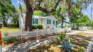 A two-story house with a white picket fence, a large tree with Spanish moss, and a well-maintained lawn. - Historic St Andrews Private Coastal Bungalow 3 bedroom Sleeps 8 (Panama City)