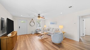 A modern living room with a flat-screen TV, ceiling fan, and a sofa. - Historic St Andrews Private Coastal Bungalow 3 bedroom Sleeps 8 (Panama City)