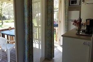 Ein Zimmer mit einer Schiebetür zum Außenbereich, einer kleinen Küchenzeile mit einer Mikrowelle und einem Esstisch mit Stühlen.