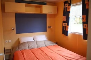 A bedroom with a bed, a headboard, a window with curtains, and a door. - Camping 3 étoiles - Piscine  - ccbgacf (Le Mas-d'Azil)