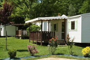 A mobile home with a porch, a small deck, and a garden with various plants. - Camping 3 étoiles - Piscine  - ccbgacf (Le Mas-d'Azil)