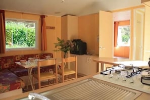 A compact kitchen with a dining area, a small table, and a sofa. - Camping 3 étoiles - Piscine  - ccbgacf (Le Mas-d'Azil)