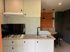 A compact kitchen with a gas stove, a sink, and a small dining area with a chair. - Camping 3 étoiles - Piscine  - ccbgdgg (Arc-et-Senans)