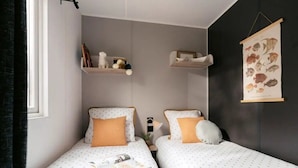 Un dormitorio con dos camas, una estantería con libros y adornos, e ilustración de un pez colgada en la pared.