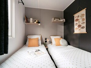 A bedroom with two beds, a shelf with books and decorative items, and a wall-mounted fish illustration. - Camping 3 étoiles - Piscine  - ccbgdgg (Arc-et-Senans)