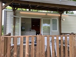 A covered deck area with a wooden railing, a white plastic chair, and a small table. - Camping 3 étoiles - Piscine  - ccbgdgg (Arc-et-Senans)
