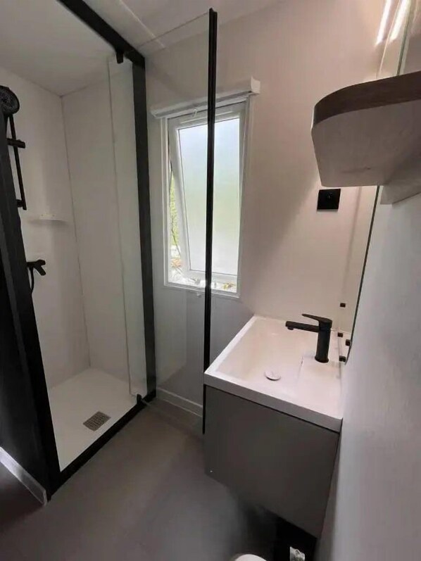 Une salle de bain moderne avec une douche à parois de verre, un lavabo blanc et un miroir.