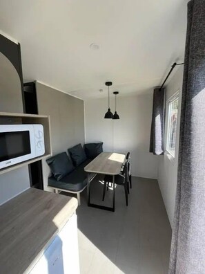 En kompakt opholdsstue med tekøkken, spiseplads og siddeområde.