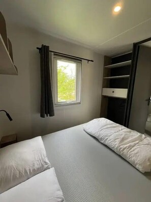 A bedroom with a bed, a window with curtains, a shelf unit, and a ceiling light. - Camping 3 étoiles - Piscine  - ccbgdgh (Arc-et-Senans)