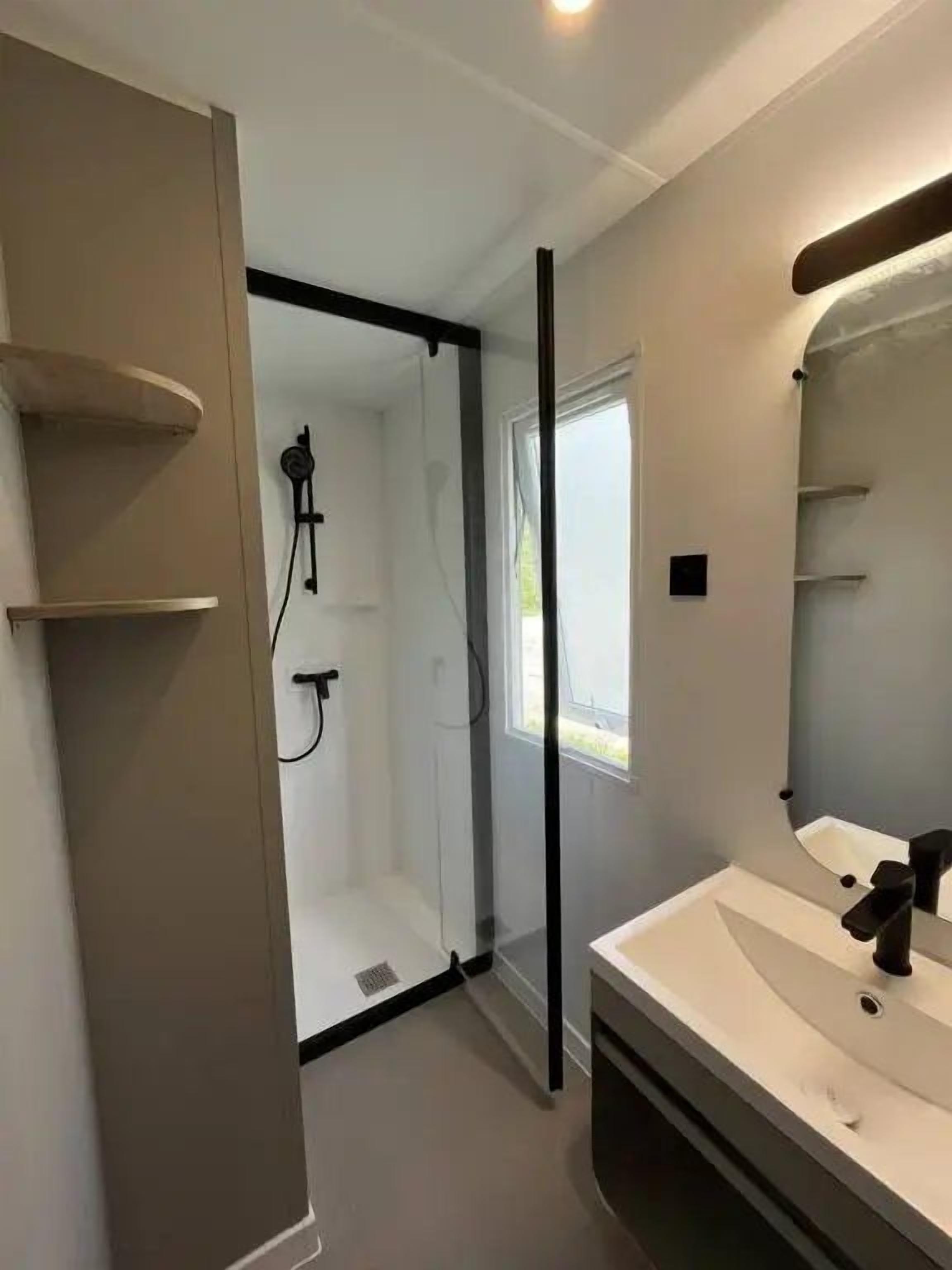 A modern bathroom with a glass shower enclosure, a white sink, and a mirror.