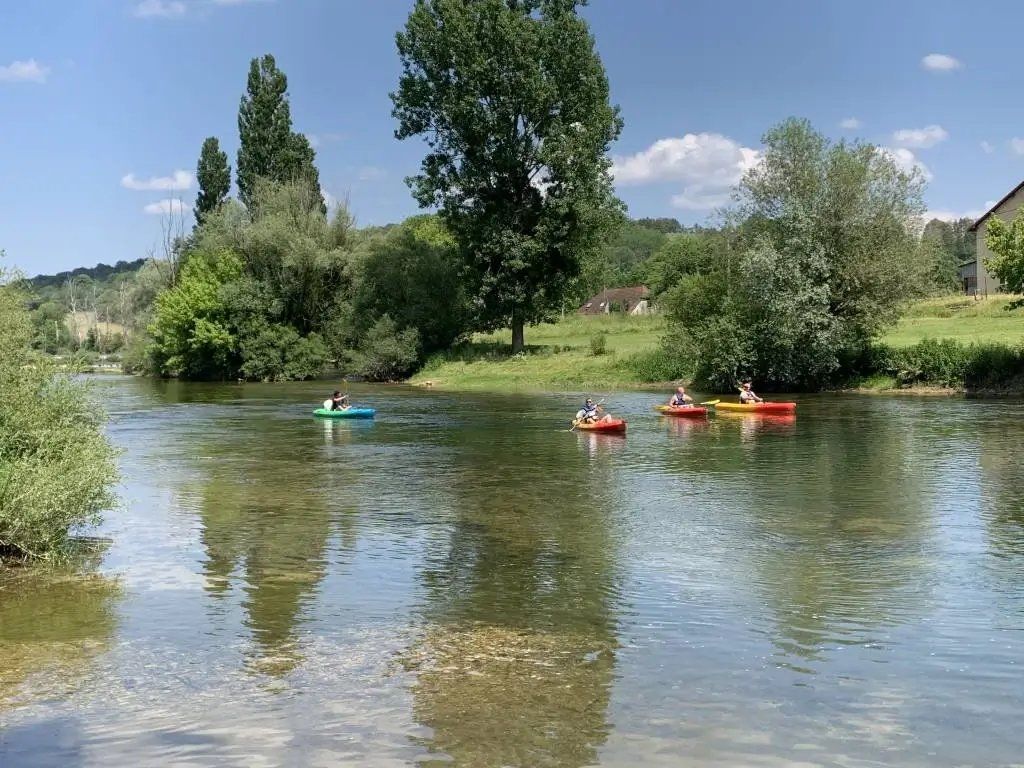 A calm river with kayaks, surrounded by trees and a building in the background.