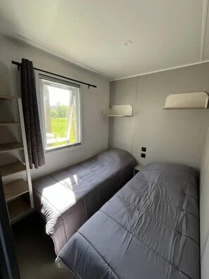 Un dormitorio con dos camas, una ventana con cortinas, una estantería y una escalera.